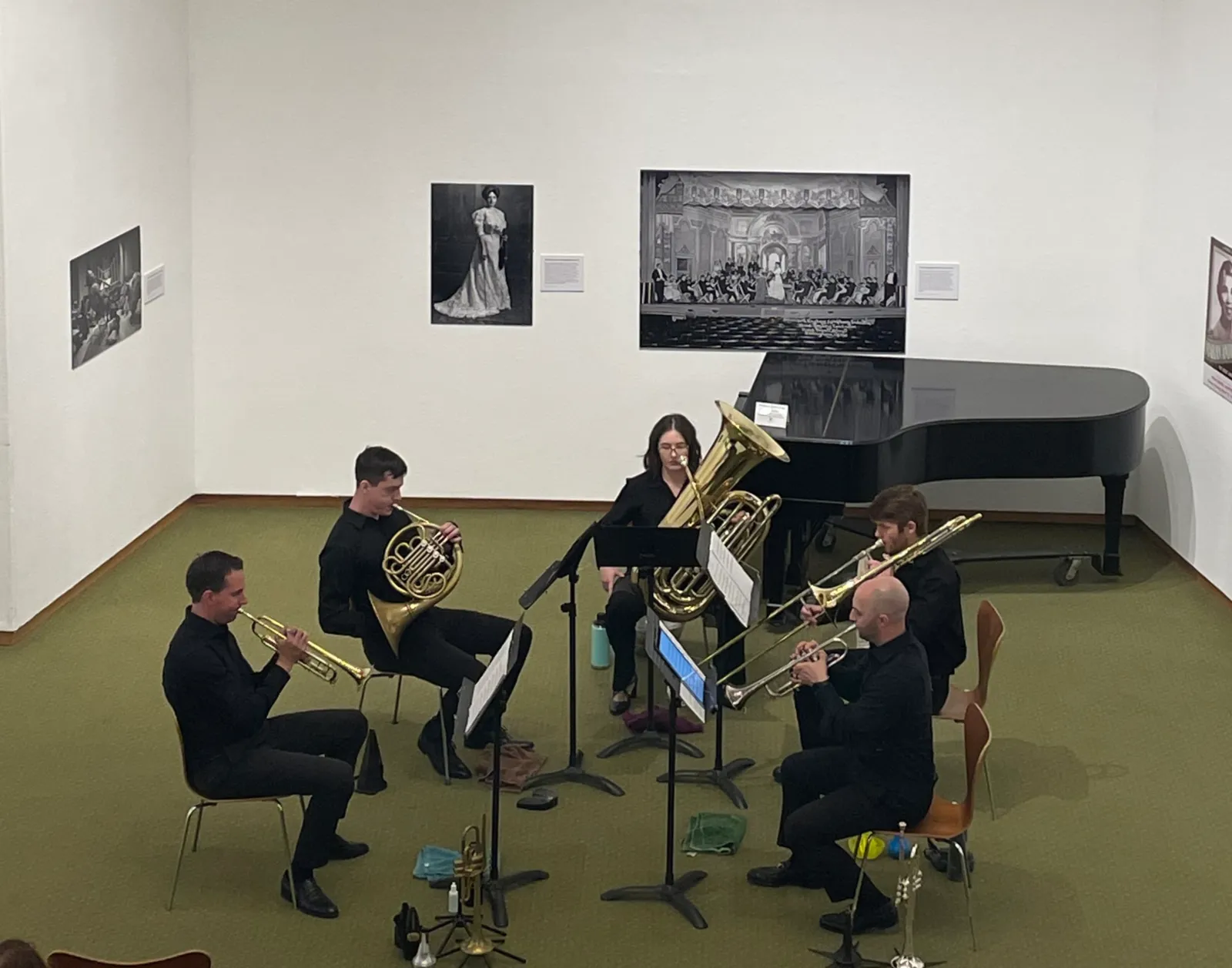 Olympus Brass musicians performing at the Whatcom Museum — trumpets, horn, and trombone raised beside a grand piano.